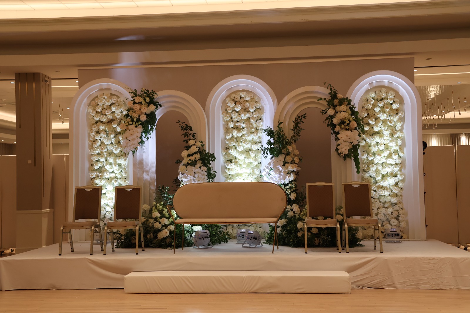 An arched floral stage with a settee and chairs