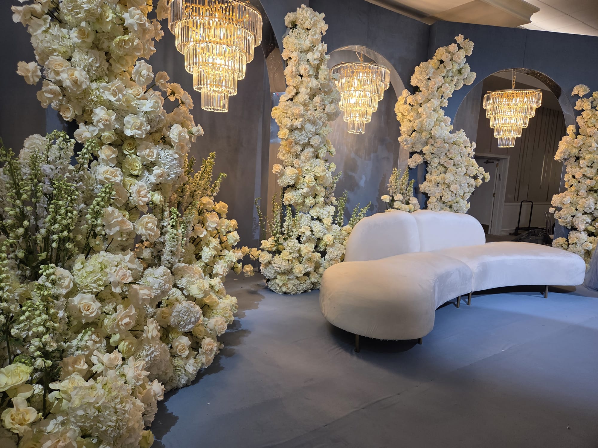 A curved lounge seat surrounded by white blossoms and chandeliers
